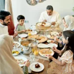 Multi-generation Saudi men in dish dash, women in abaya and hijab, and children in casual western clothing, enjoying traditional dishes.